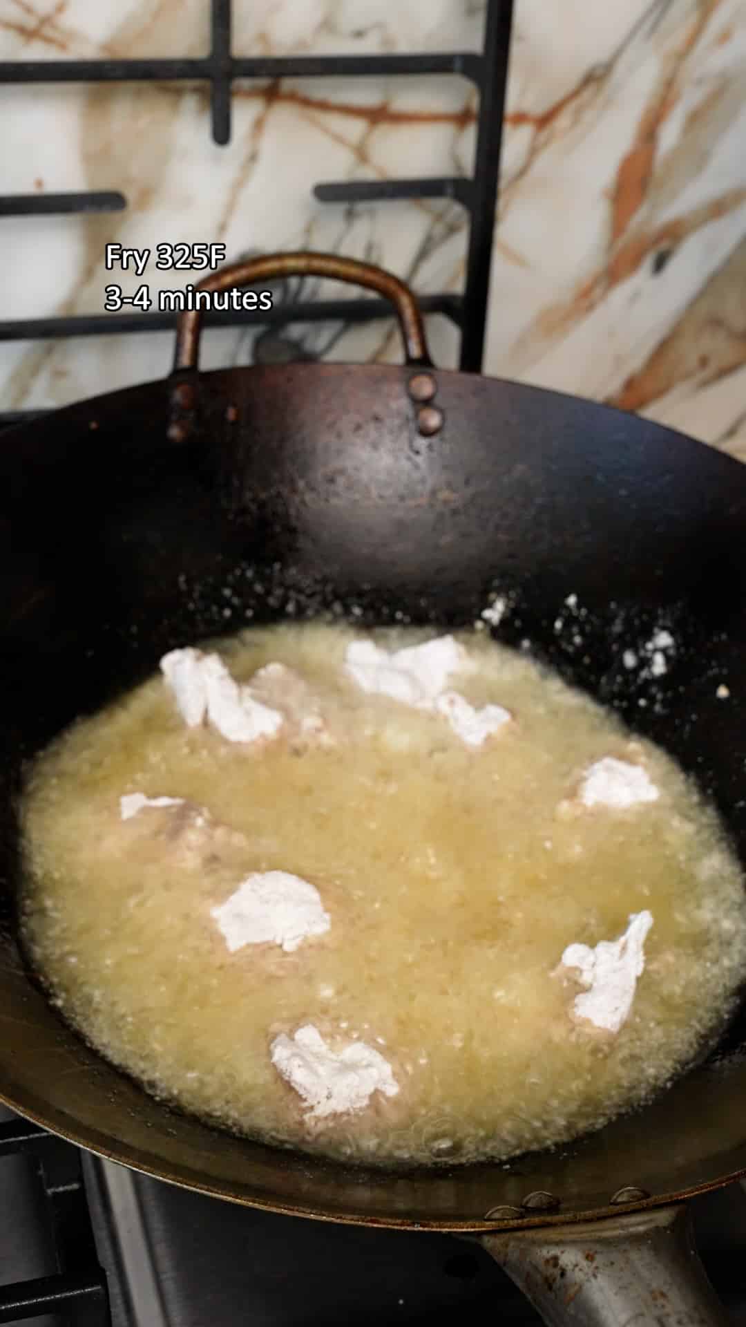 Chicken pieces frying in oil in a wok.