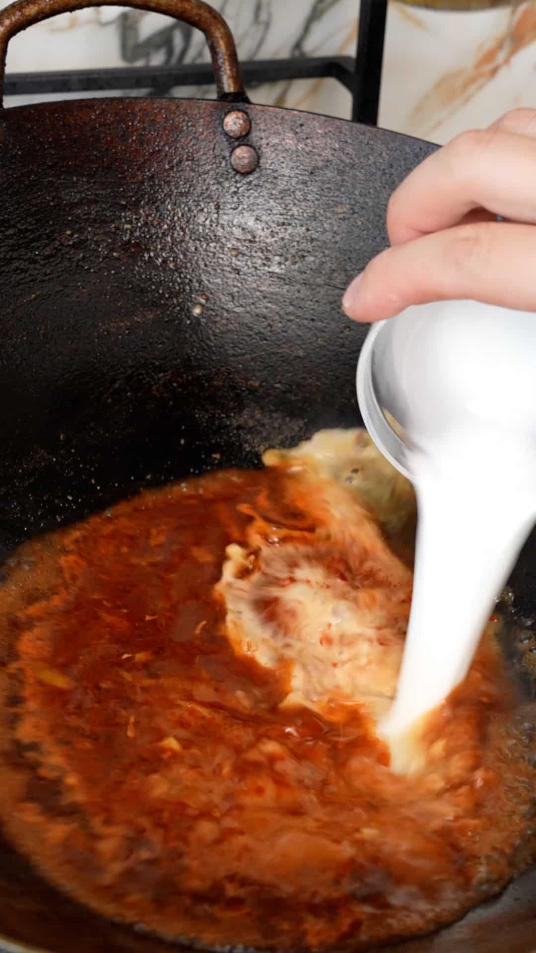 Cornstarch slurry being added to the General Tso's Chicken sauce in a wok.