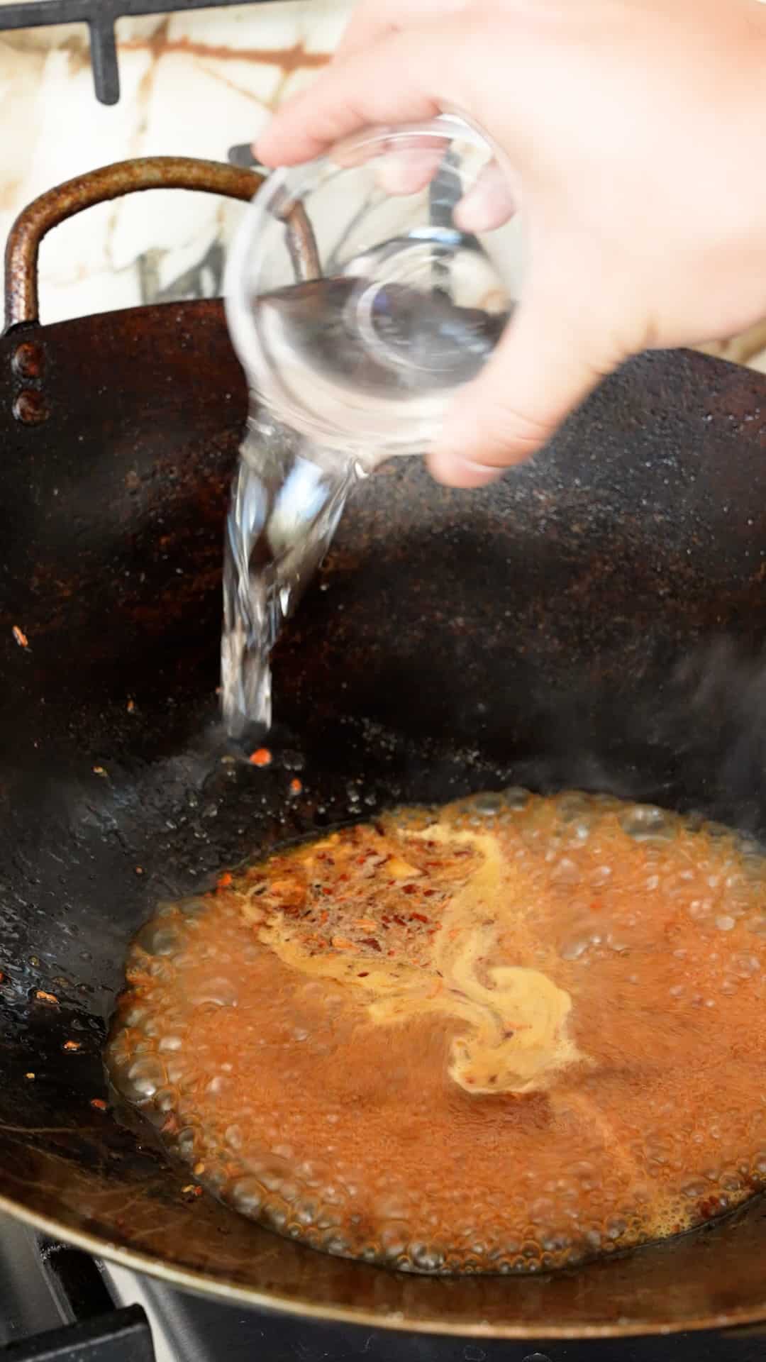 White vinegar being added to the General Tso's Sauce in a wok.