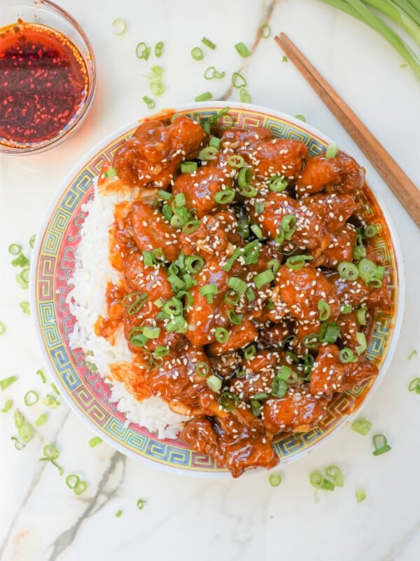 A plate of General Tso's Chicken with rice topped with scallions and sesame seeds.