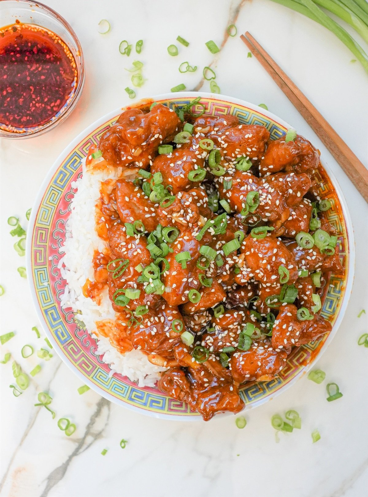 A plate of General Tso's Chicken with rice topped with scallions and sesame seeds.