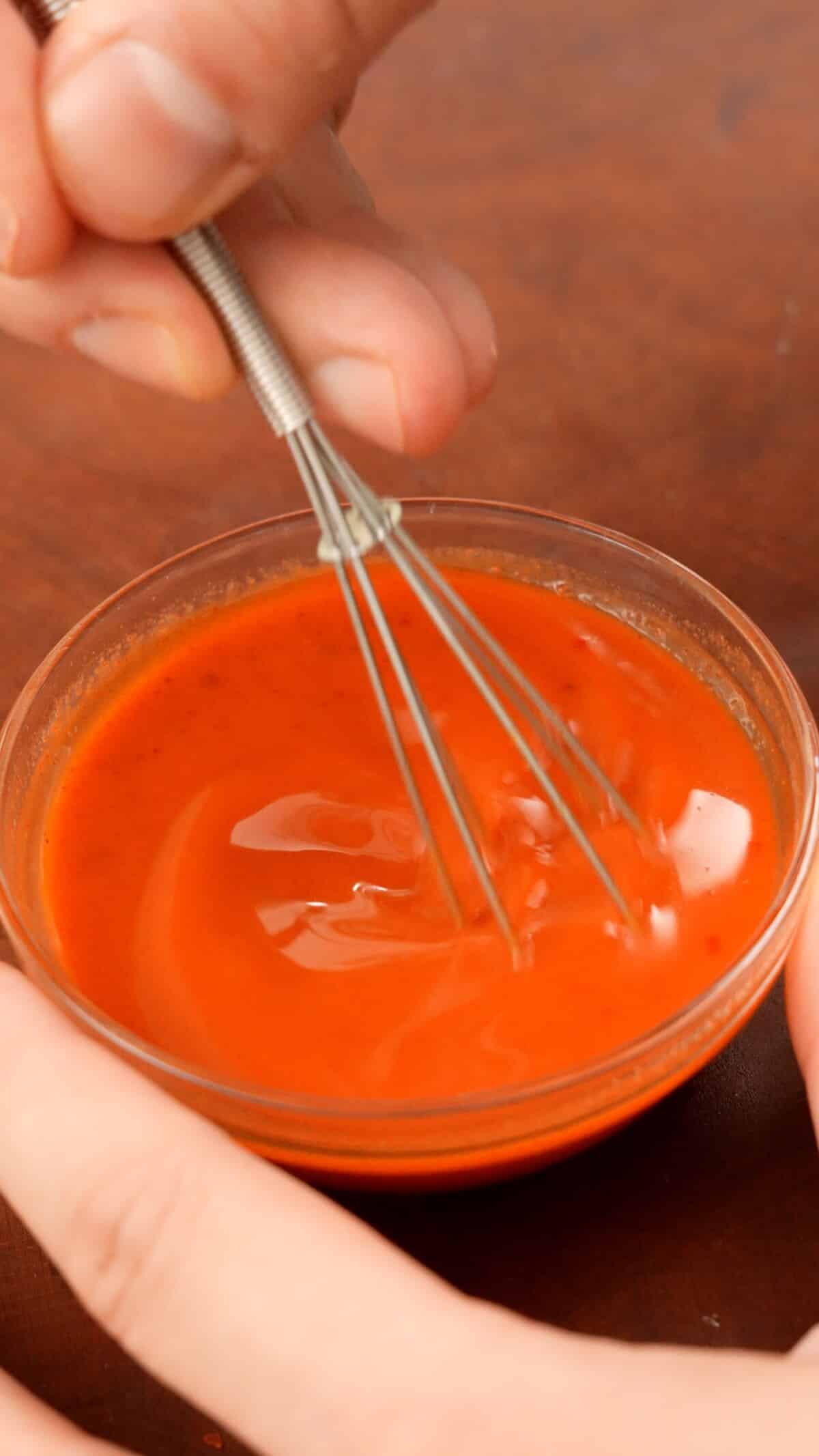 Gochujang, kimchi juice, and water mixed in a bowl with a small whisk.