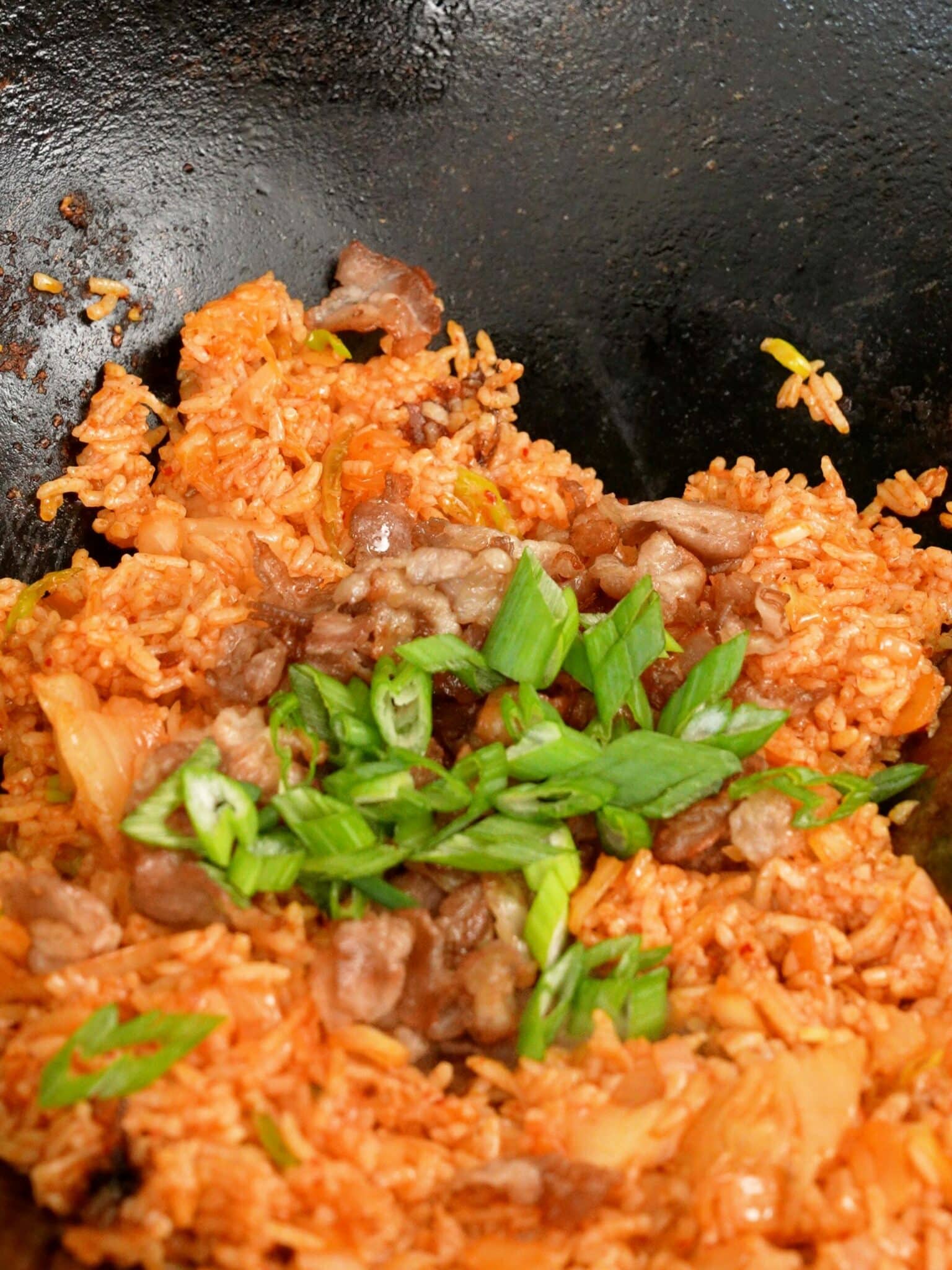 Pork belly and scallions added to kimchi fried rice in a wok.
