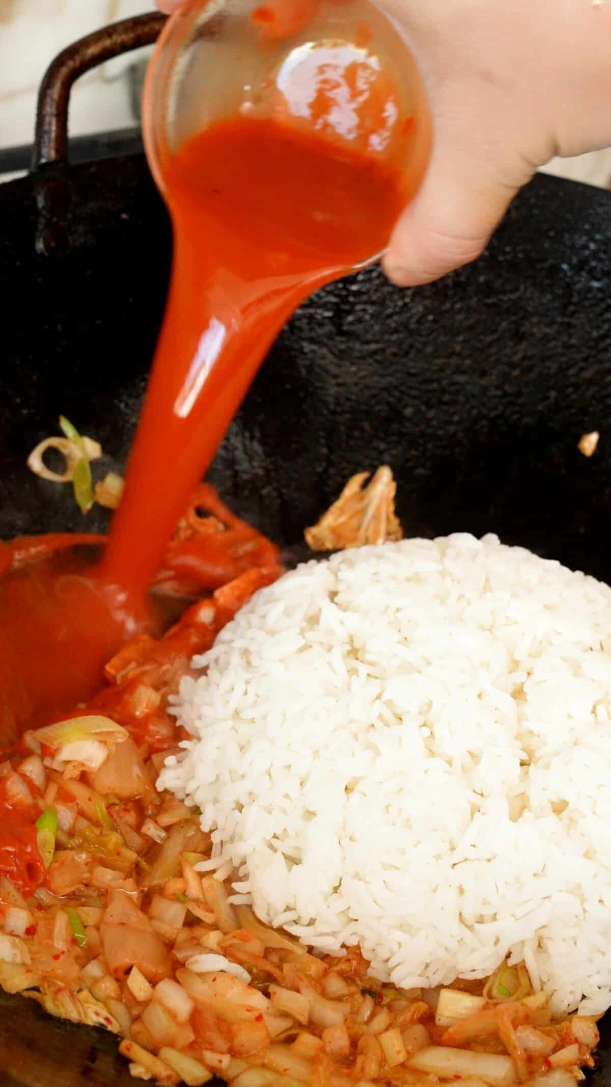 Kimchi Fried Rice sauce being poured in a wok with rice and sauteed vegetables.