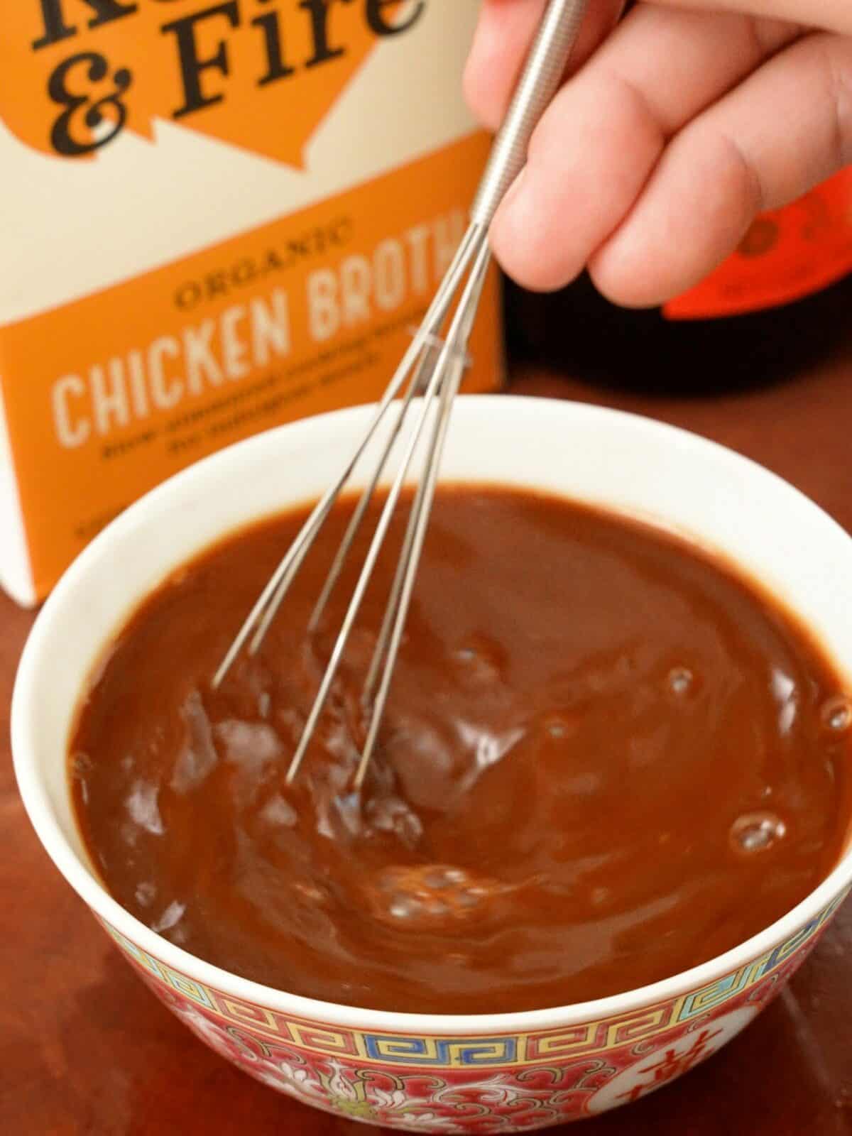 A whisk mixing kung pao chicken sauce in a bowl.