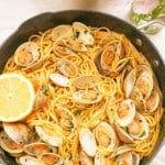 Linguine with clams in a pan topped with lemon and fresh parsley.