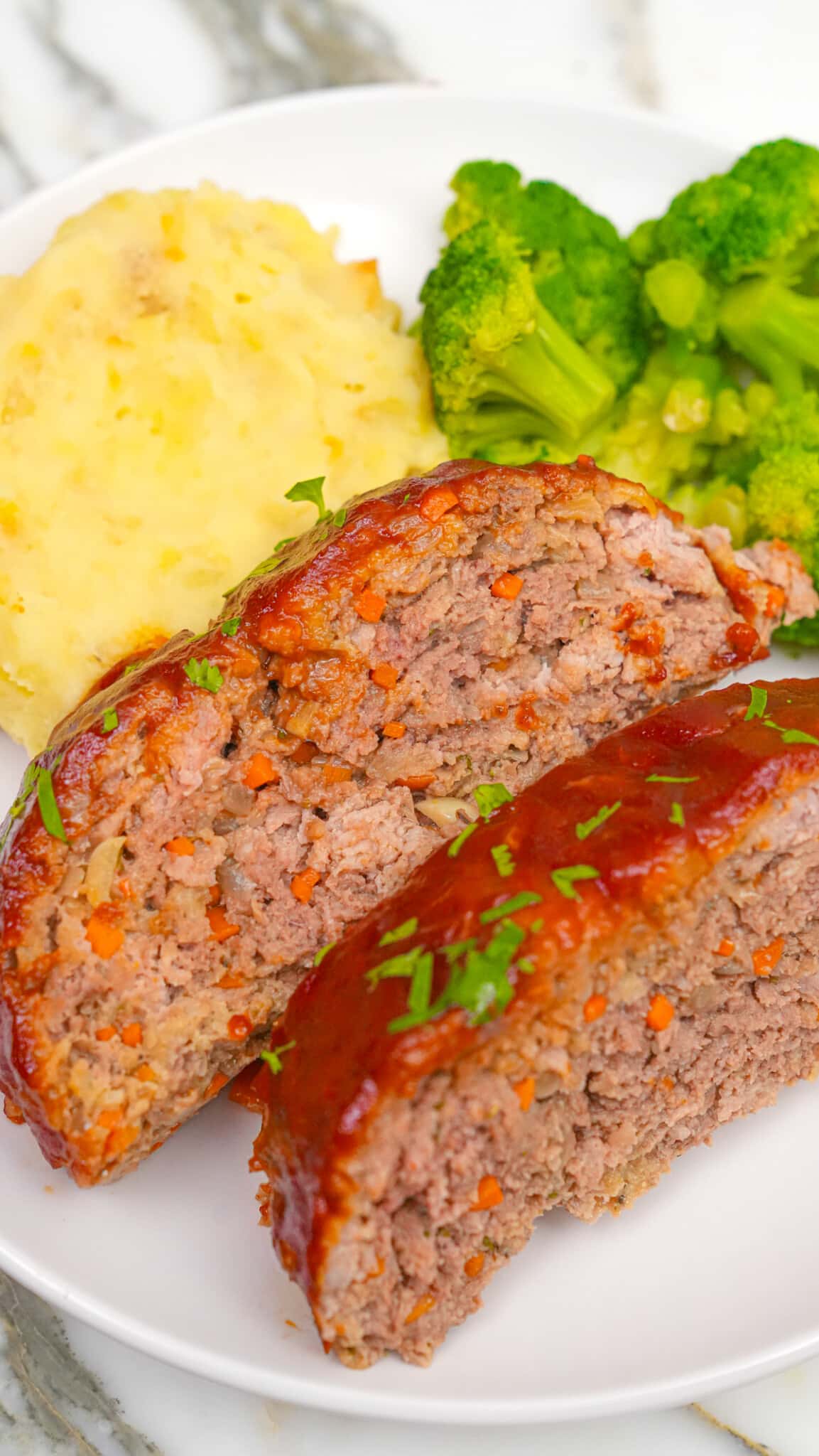Sliced meatloaf on a plate with broccoli and mashed potatoes.