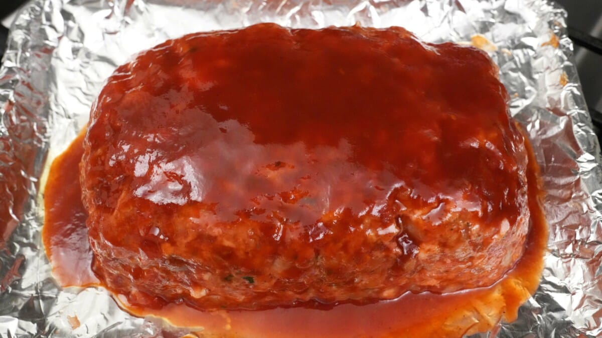 Meatloaf brushed with glaze on a foil lined baking sheet.
