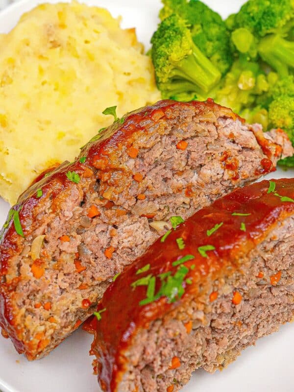 A plate of meatloaf slices with mashed potatoes and broccoli.