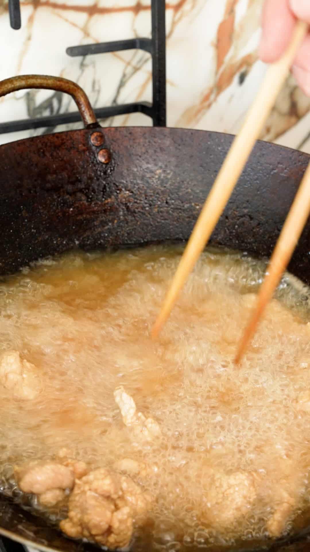 Chicken pieces frying in hot oil in a wok.