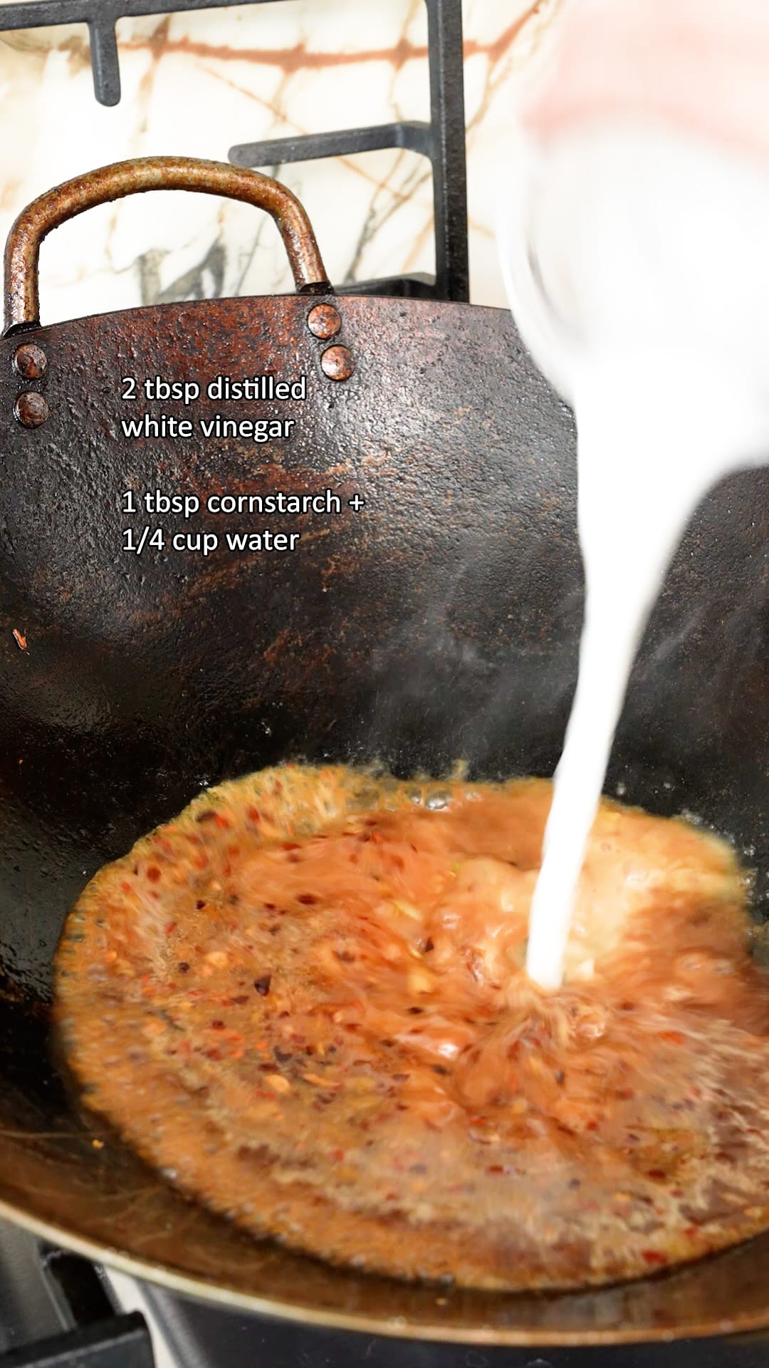 Adding cornstarch slurry to the orange sauce to thicken it in a wok.