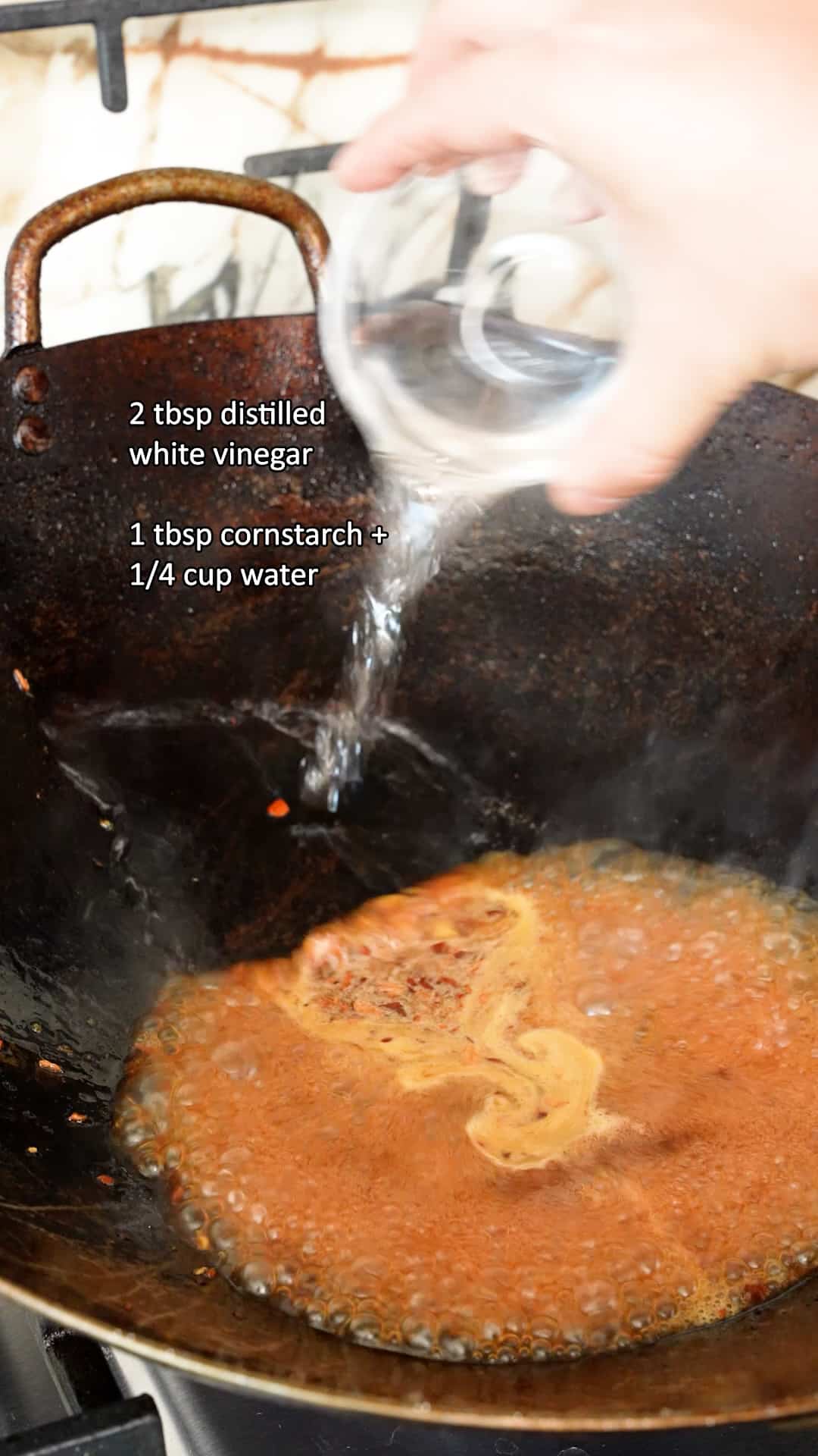 Distilled white vinegar being added to the Orange sauce in a wok.