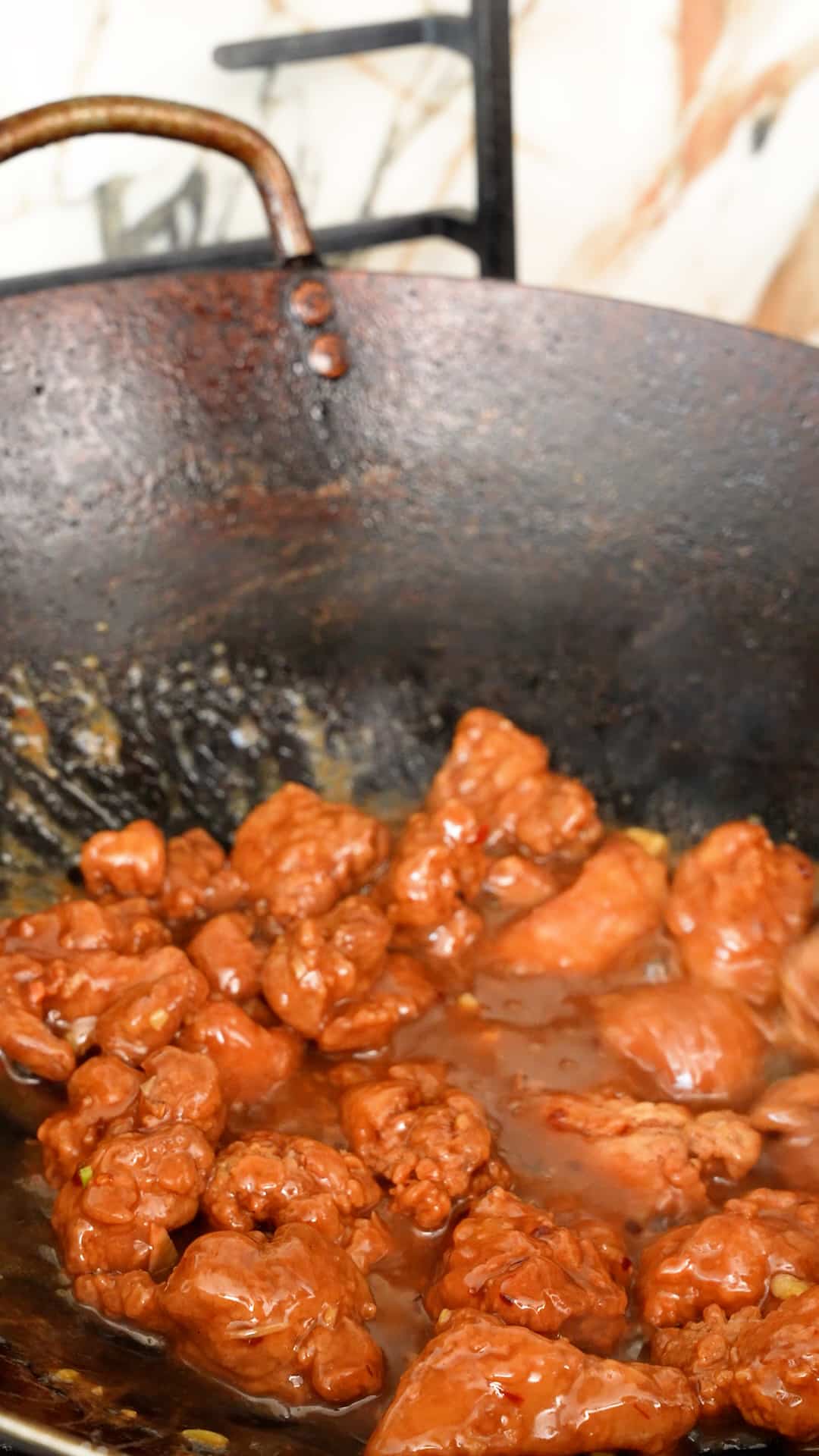 Crispy chicken being tossed in Orange sauce in a wok to make Orange Chicken.