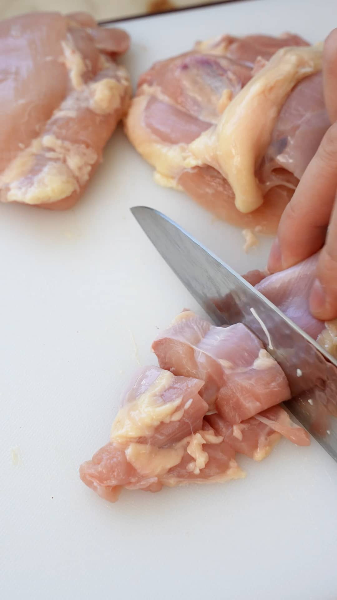 Chicken being cut into pieces with a knife on a cutting board.