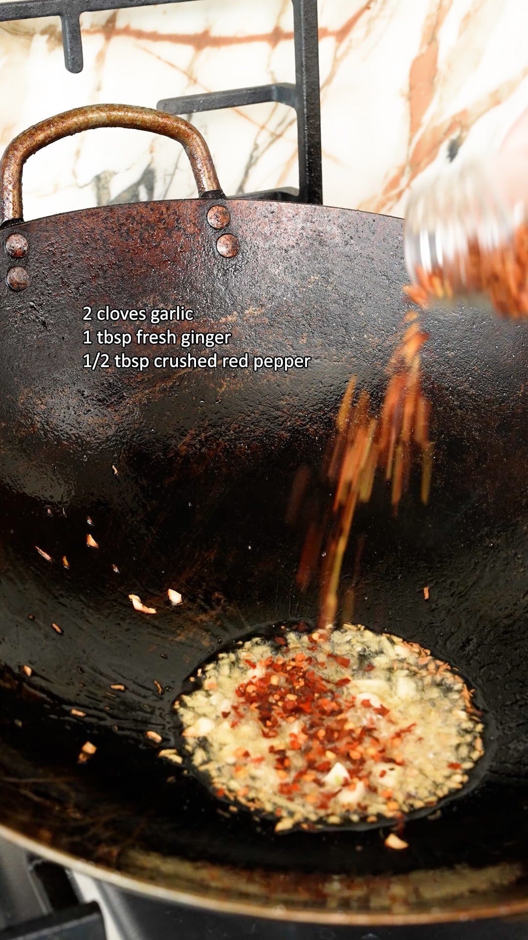 Garlic, ginger, and red pepper flakes sauteing in a wok with neutral oil.