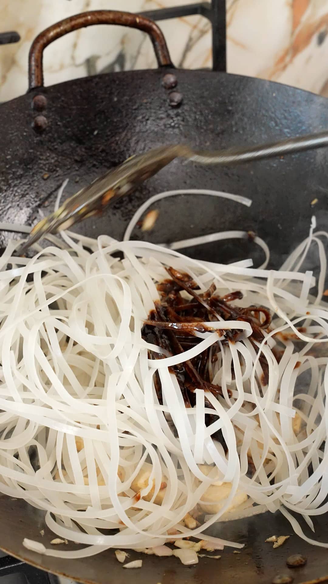 Adding rice stick noodles and pad thai sauce in a wok.