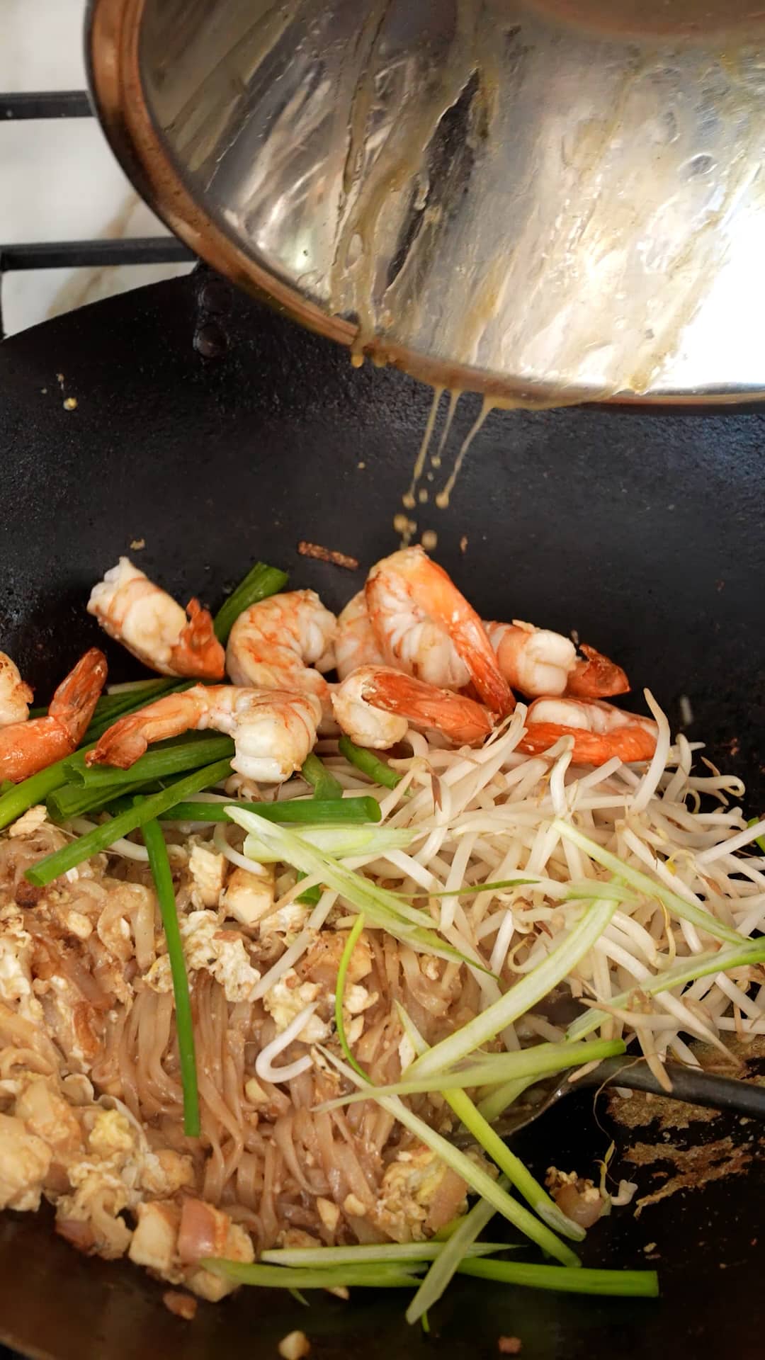 Adding cooked shrimp, bean sprouts, green onion and chopped peanuts to the Pad Thai.
