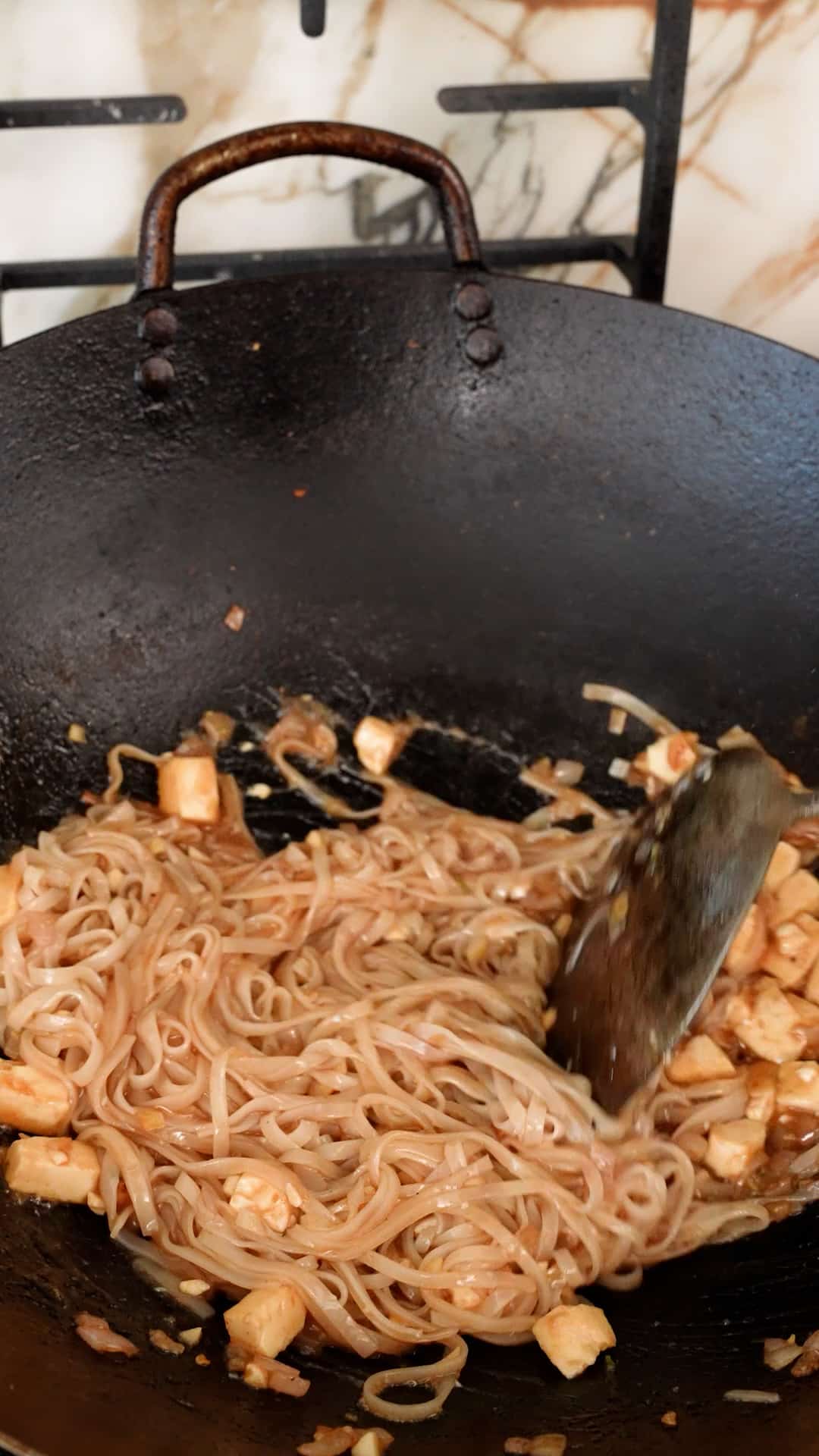 Pad thai noodles combined with pad thai sauce in a wok.