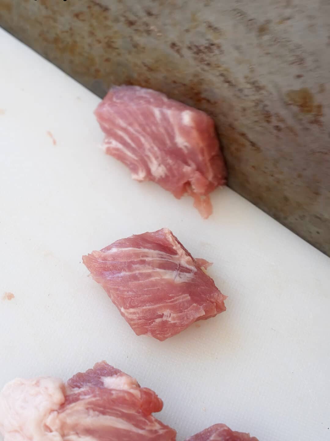 A knife slicing pork shoulder into strips against the grain.