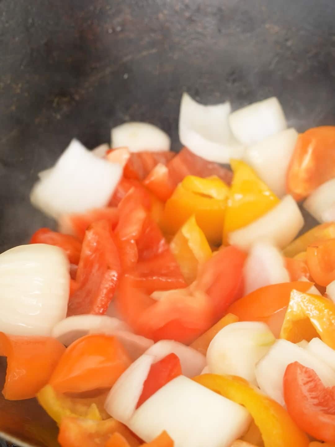 Bell peppers and onions cooking in a wok.
