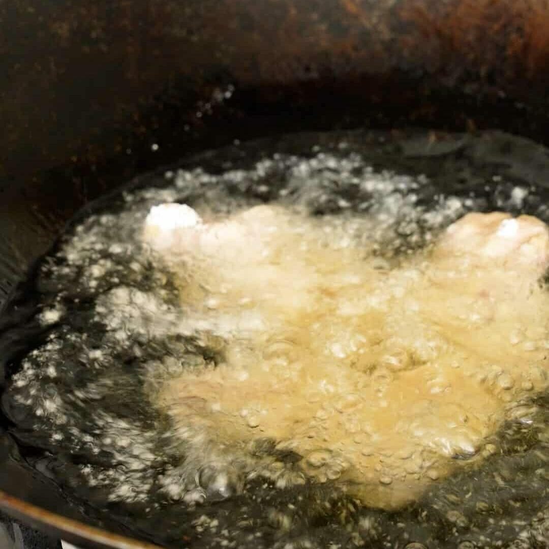 Pork pieces frying in oil in a wok.