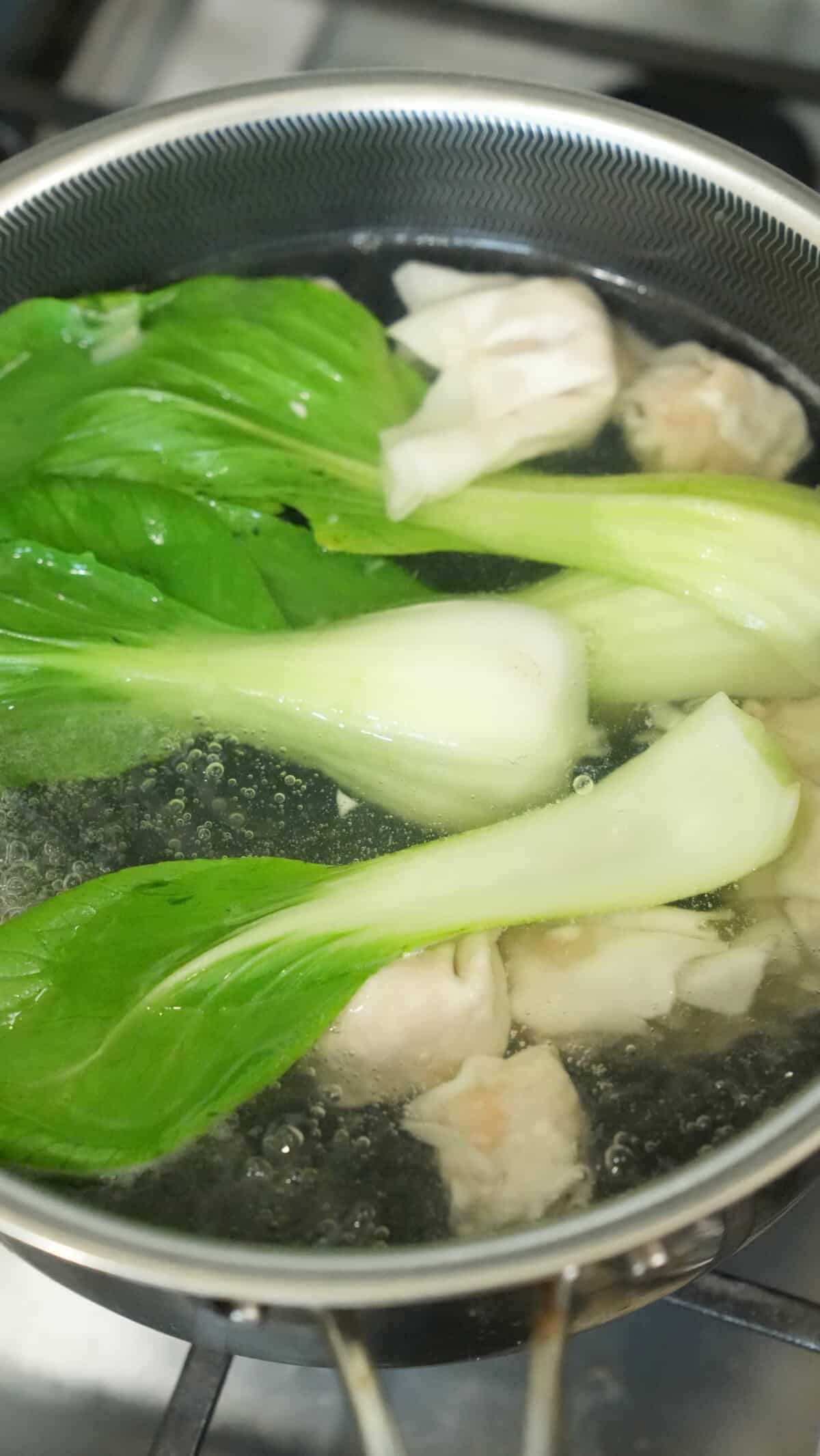 Bok choy blanching in a pot of water with wontons.