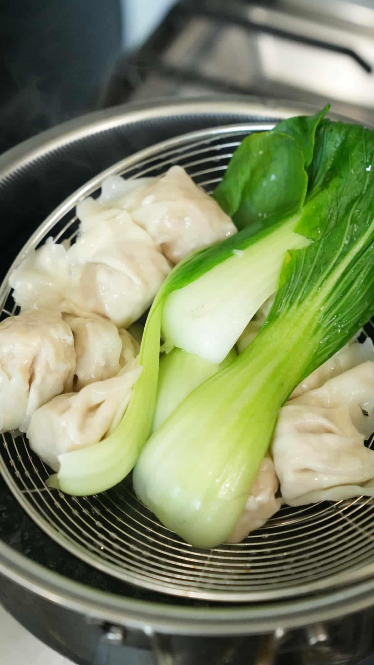Wontons and bok choy being strained out of a pot of boiling water.