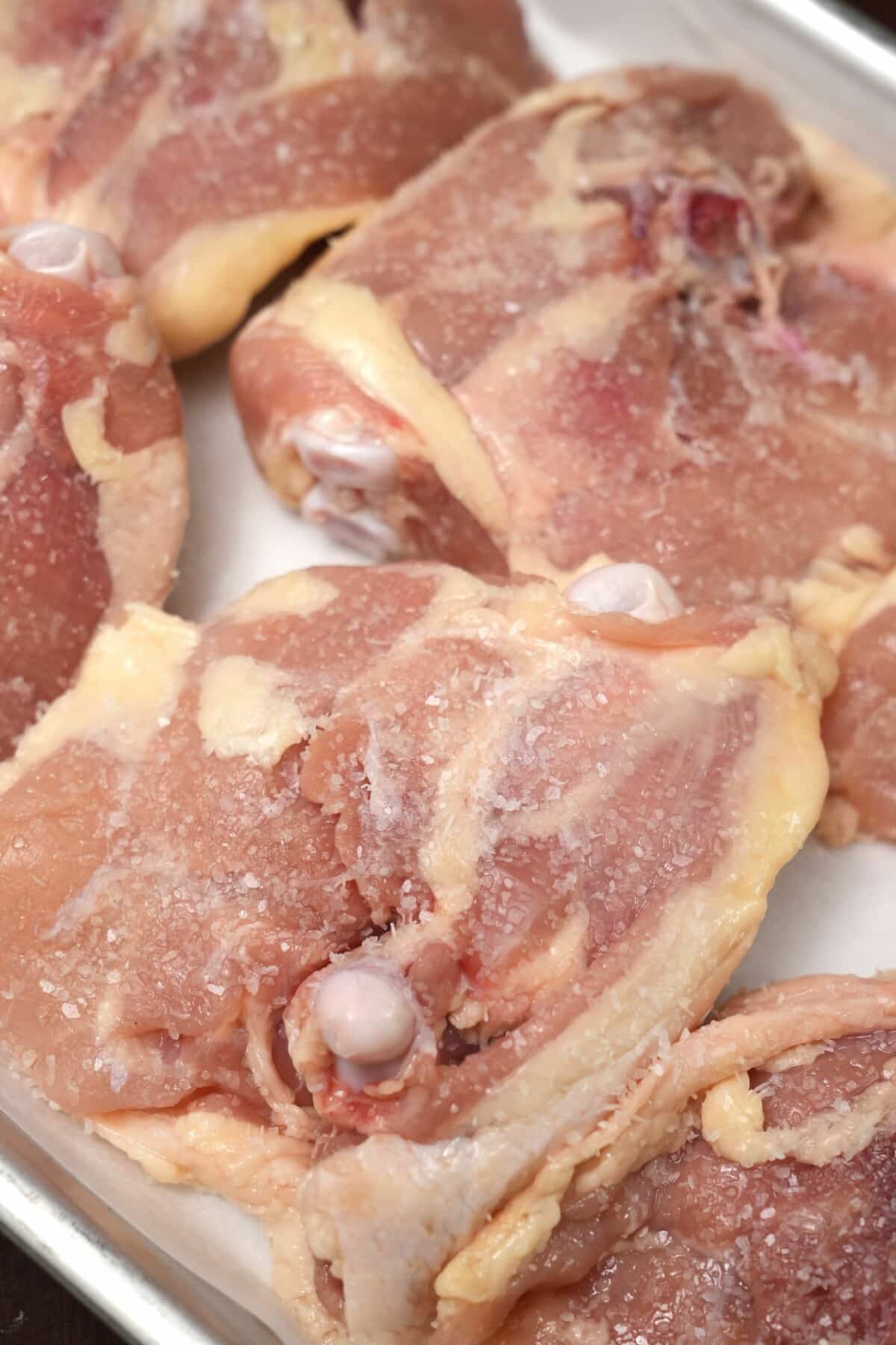 Bone-in chicken thighs skin side down on a tray seasoned with kosher salt on the meat side.