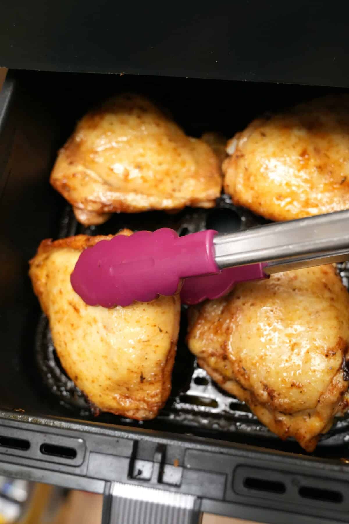 Chicken thighs being flipped skin side up in the air fryer.