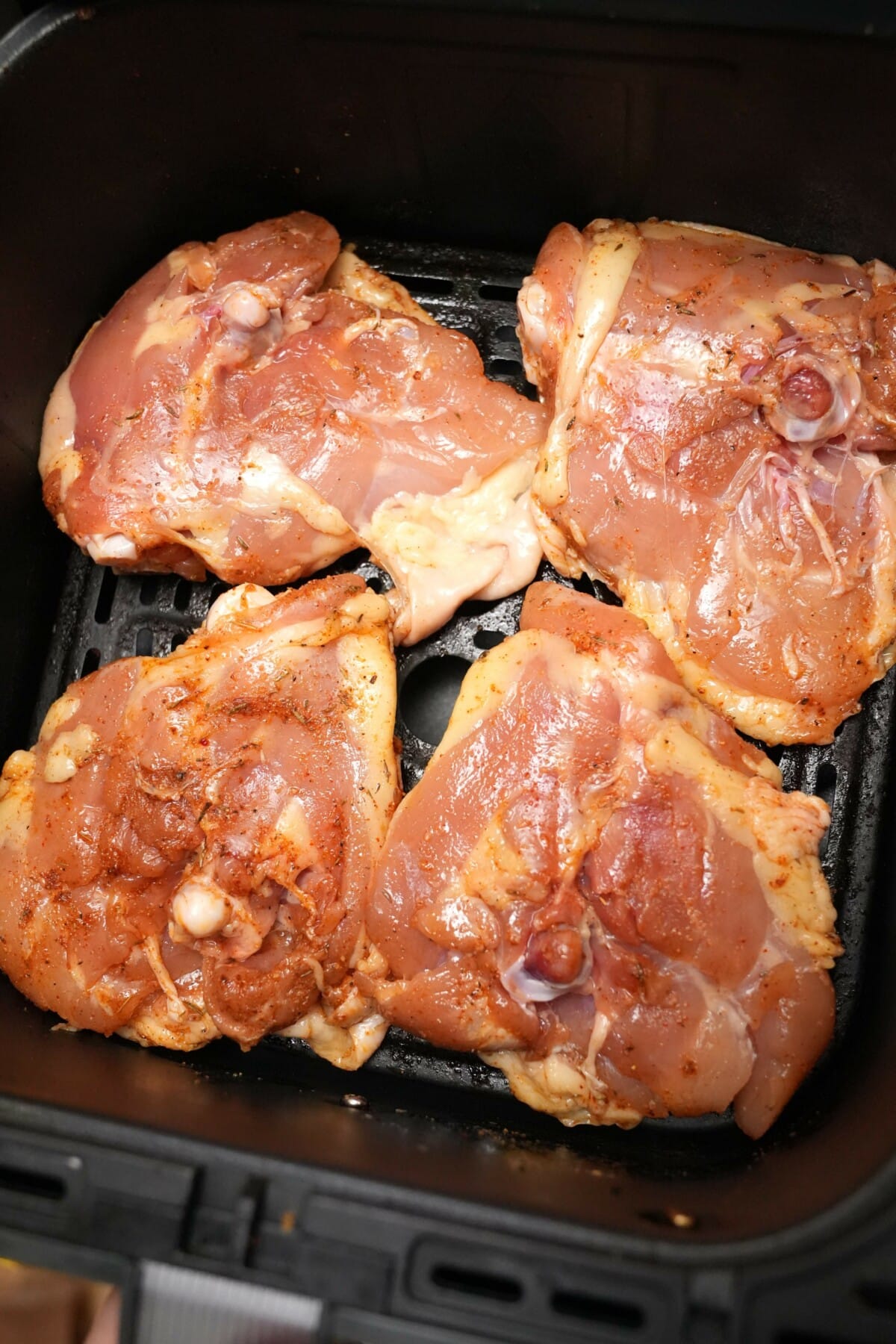 Chicken thighs skin side down in an air fryer basket.