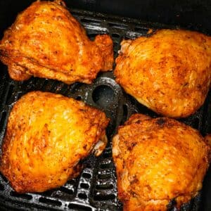 Cooked air fryer chicken thighs with crispy skin in the air fryer basket.
