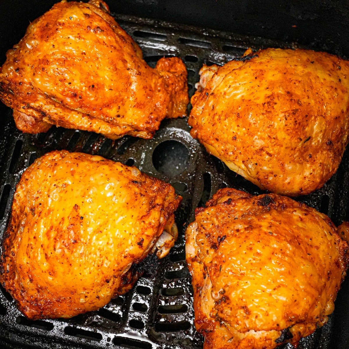 Cooked air fryer chicken thighs with crispy skin in the air fryer basket.