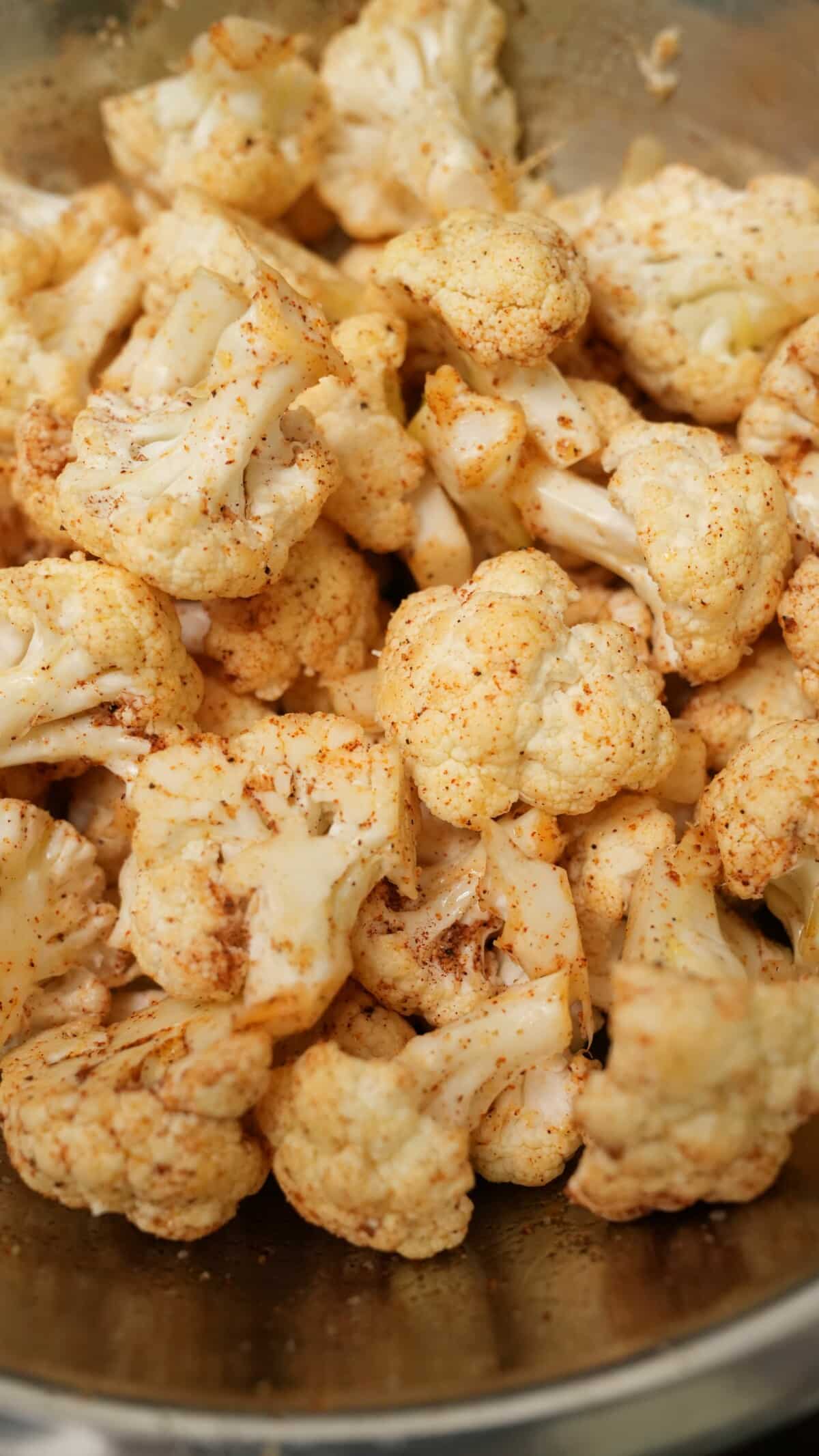 Cauliflower florets seasoned in a bowl with spice and olive oil.