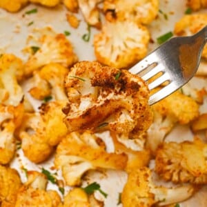 A piece of roasted cauliflower on a fork over a tray of cooked cauliflower.