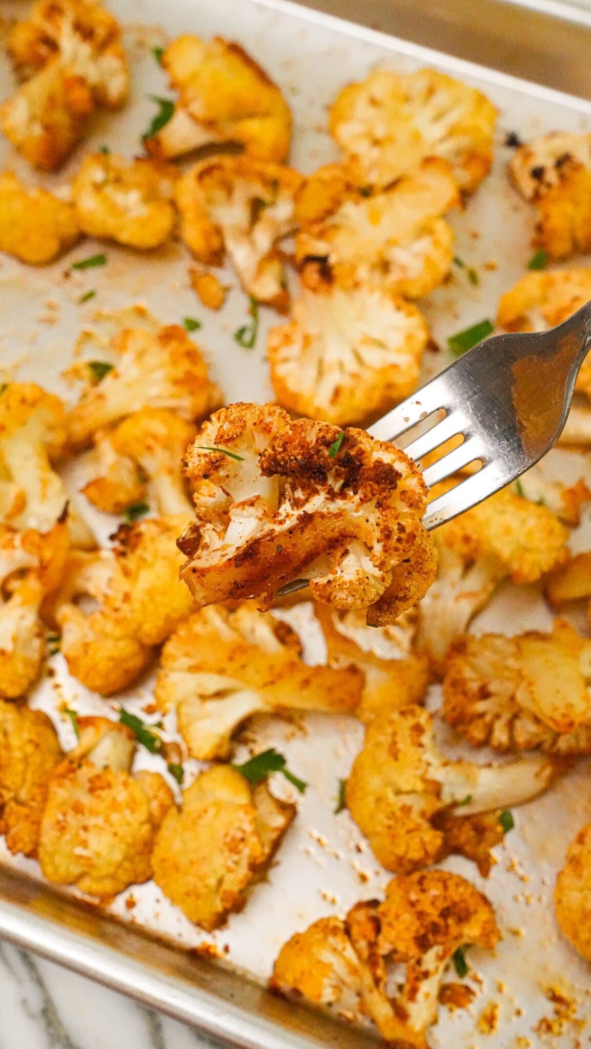 A piece of roasted cauliflower on a fork over a tray of cooked cauliflower.