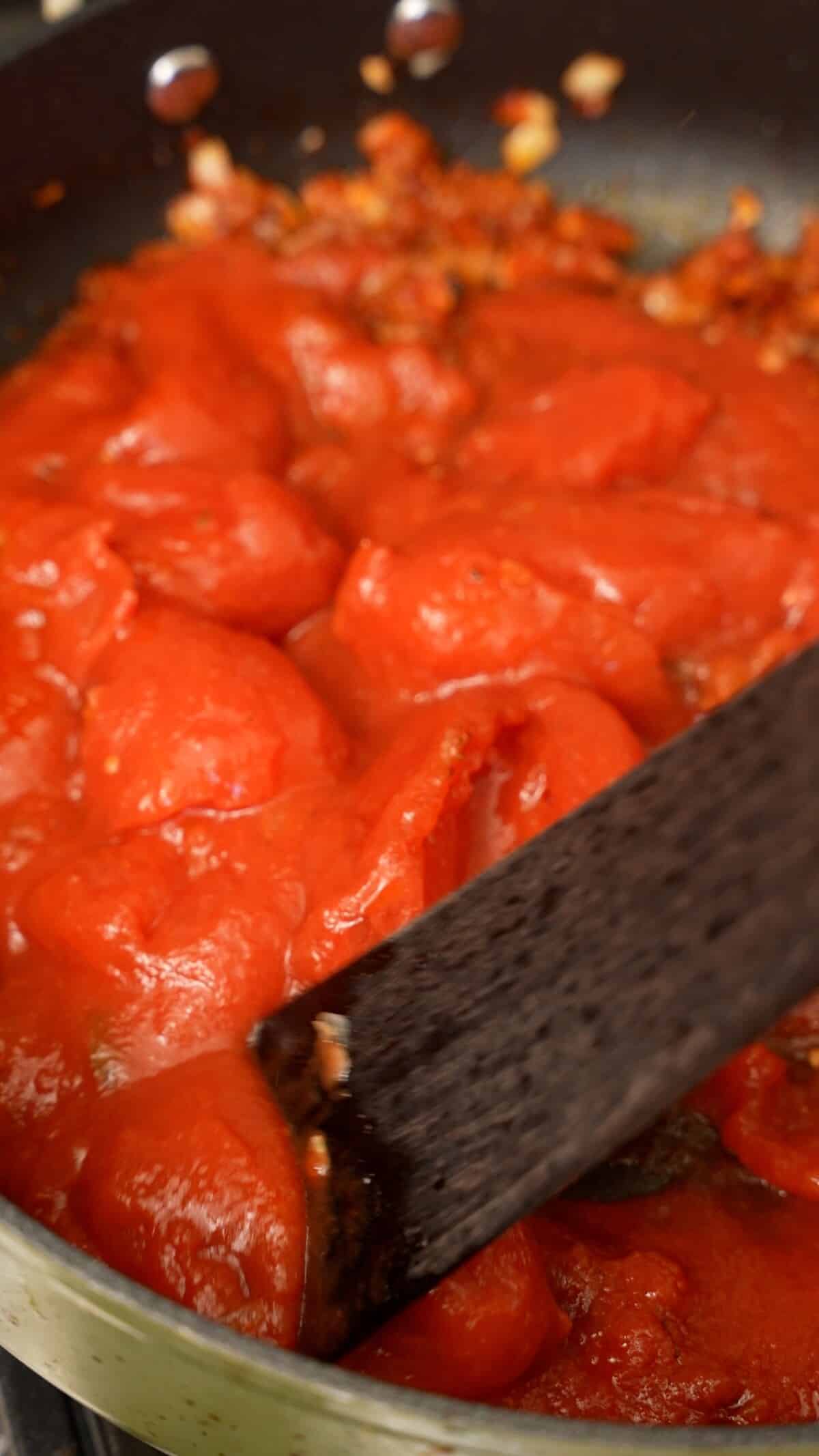 Crushing San Marzano tomatoes in a pan.