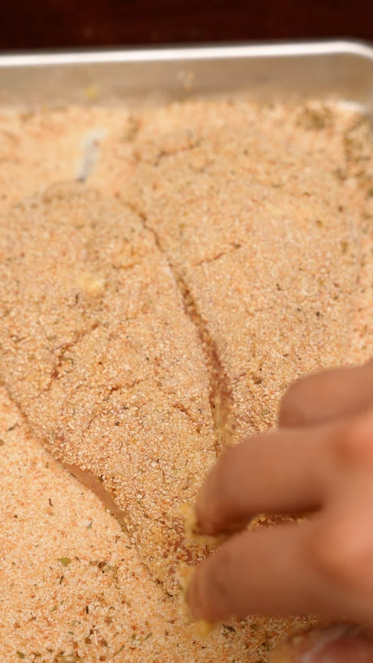 Dredging a chicken cutlet in seasoned breadcrumbs.