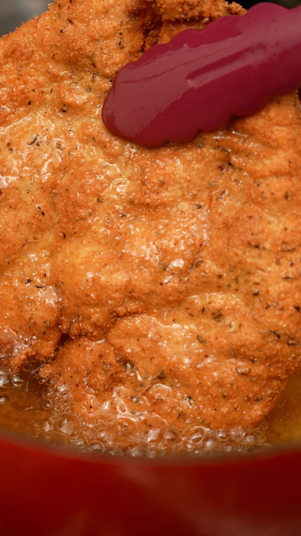 Chicken cutlet being deep fried in oil in a dutch oven.