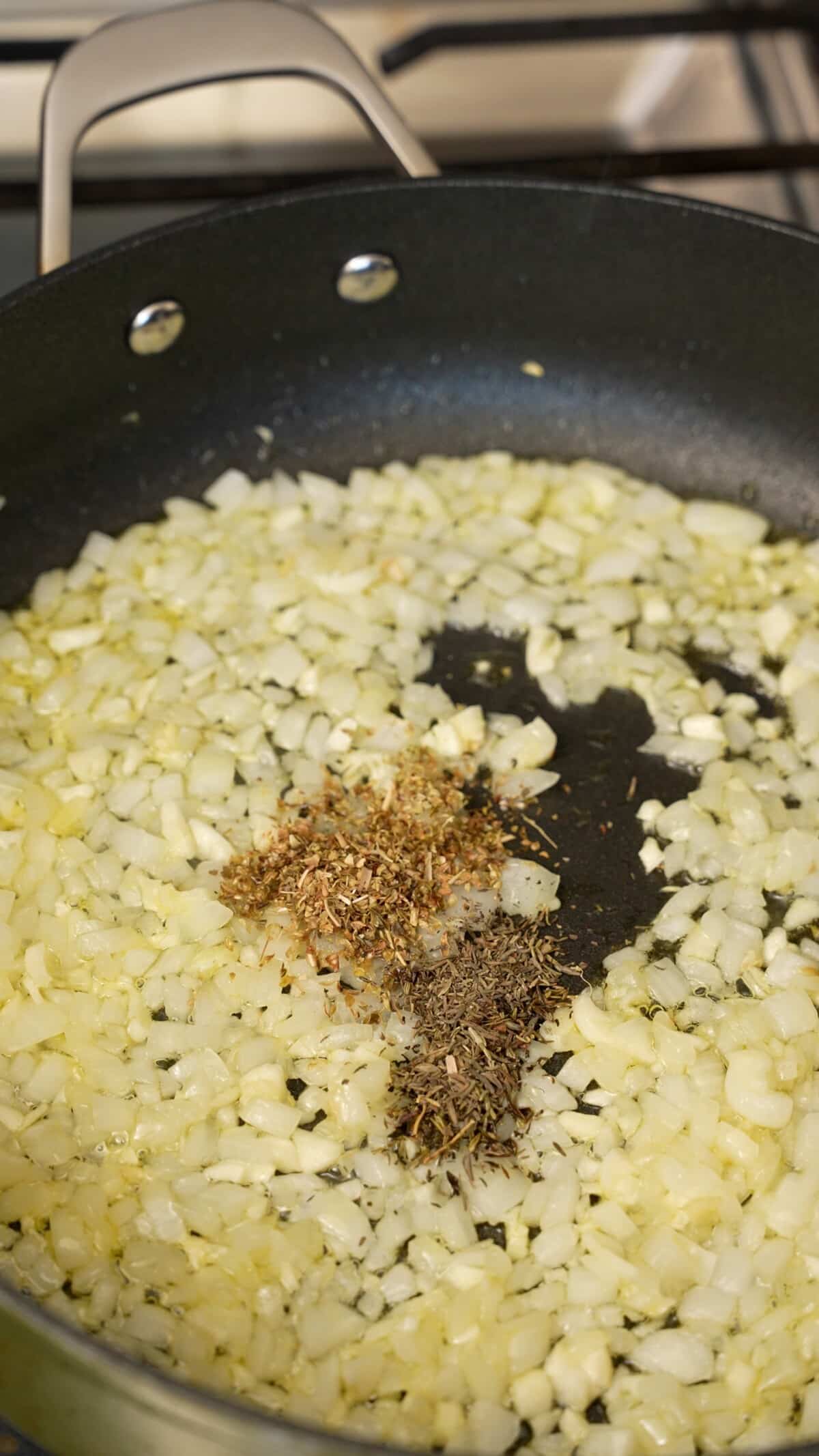 Onions, garlic, and dry seasonings sauteing in a pan with olive oil.