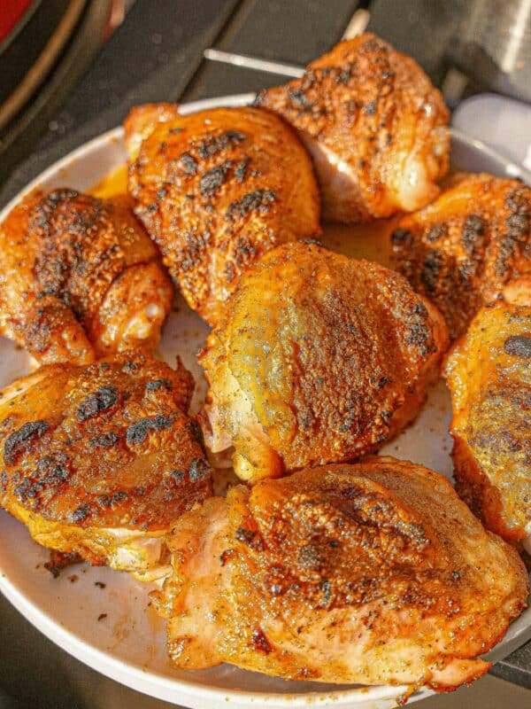 A plate of grilled chicken thighs with crispy skin and grill marks.