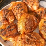 Cooked grilled chicken thighs with crispy skin on a plate.