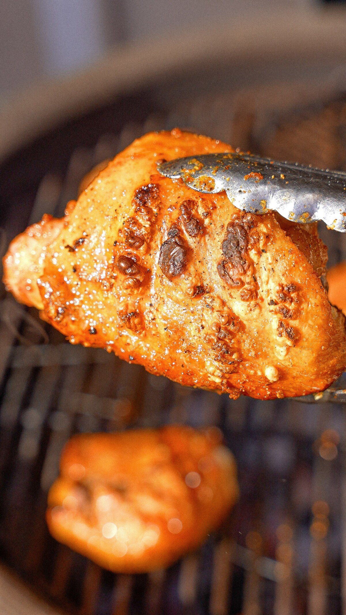 A cooked chicken thigh over a grill being held by tongs.