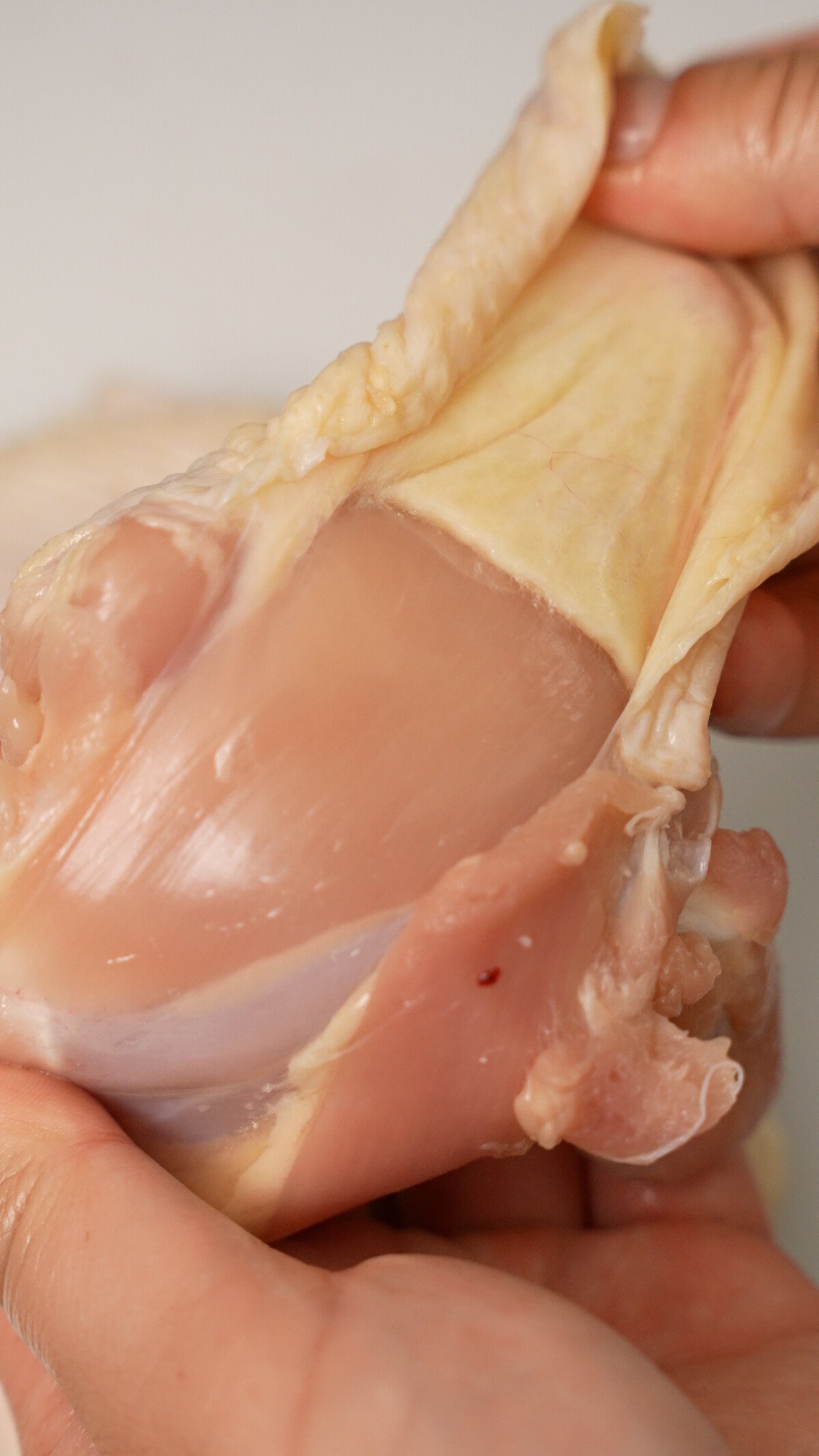 A hand pulling the skin back from the chicken thighs.