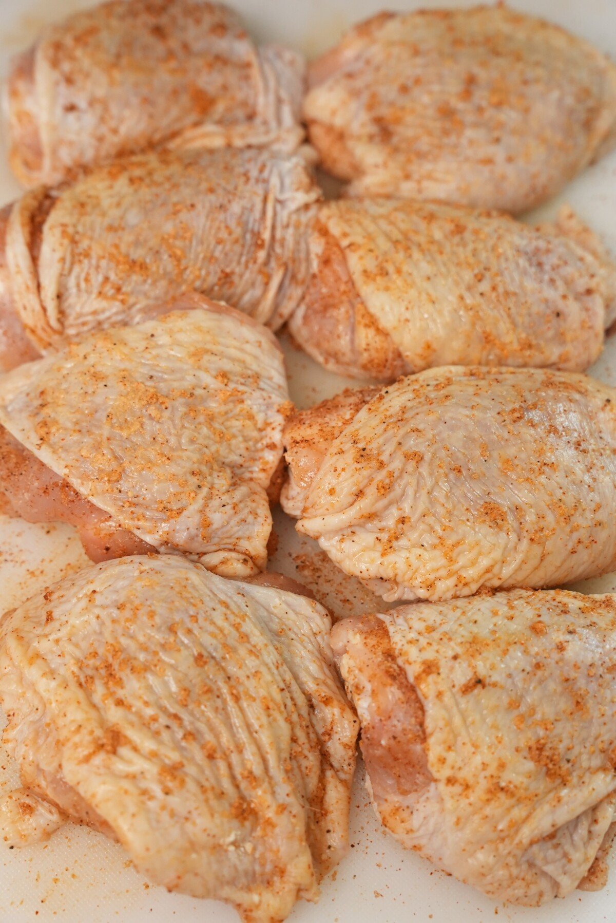 Fully seasoned chicken thighs on a cutting board.