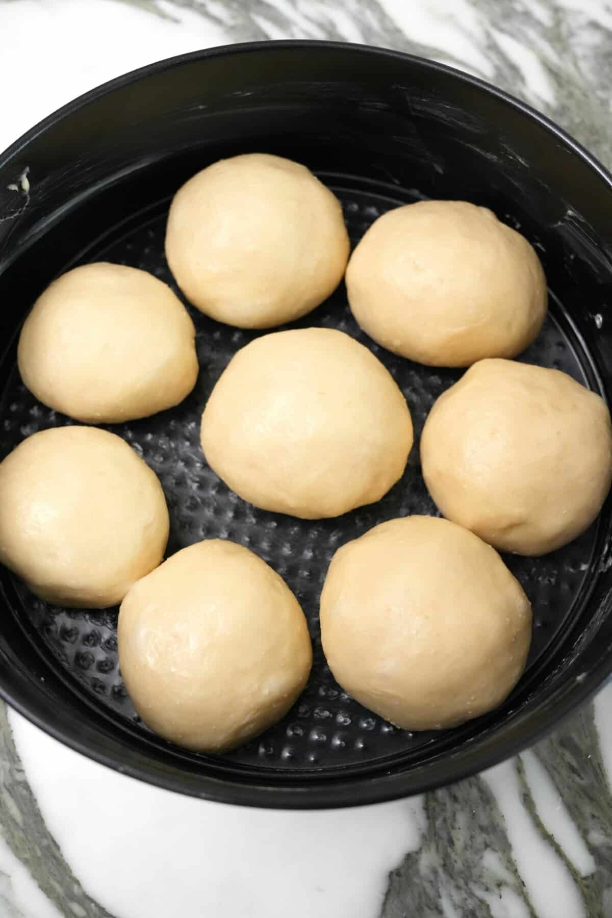 Bread dough rolled into balls and proofing in a baking tin.