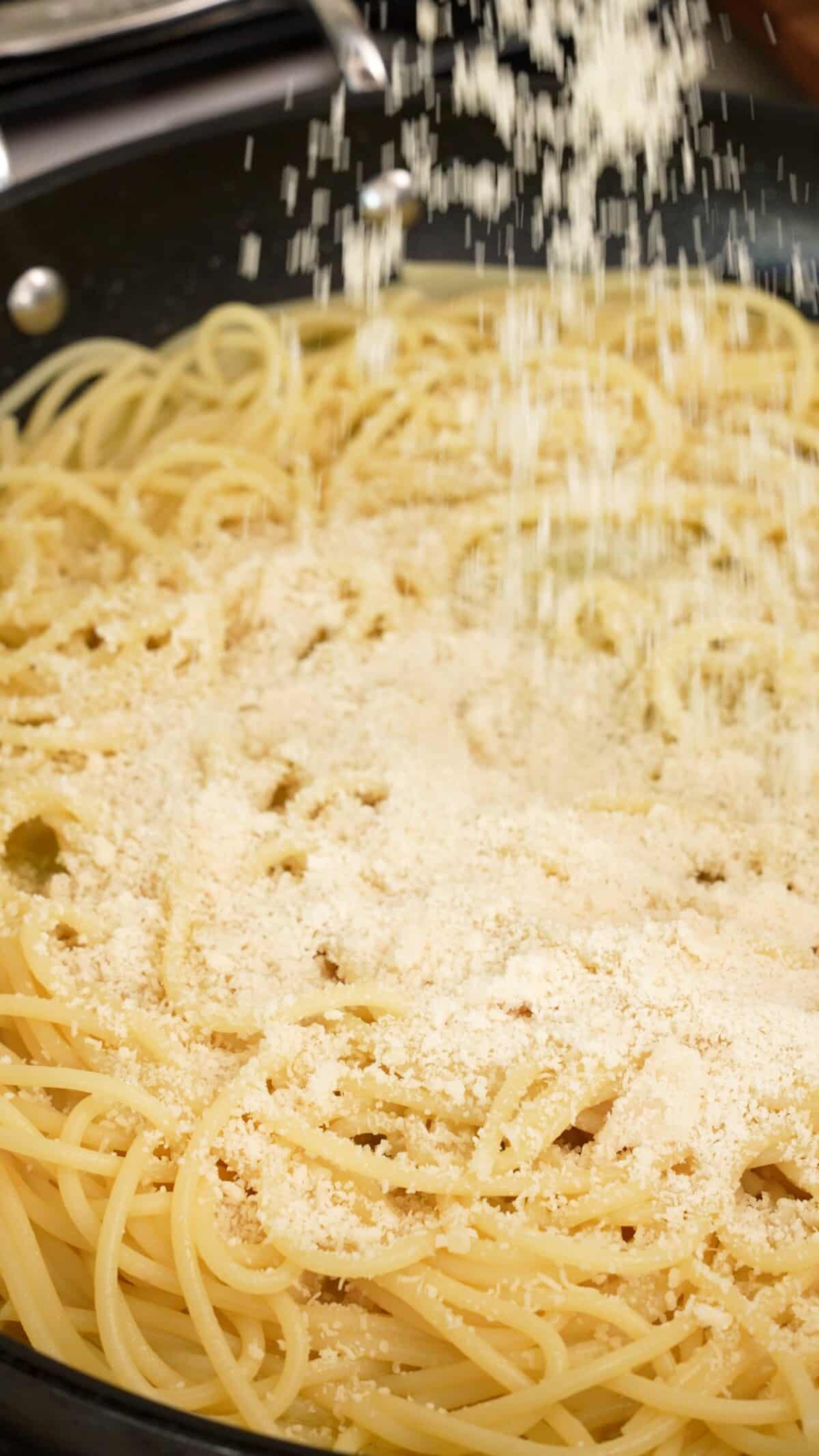 Parmesan cheese being added to pasta in a pan.
