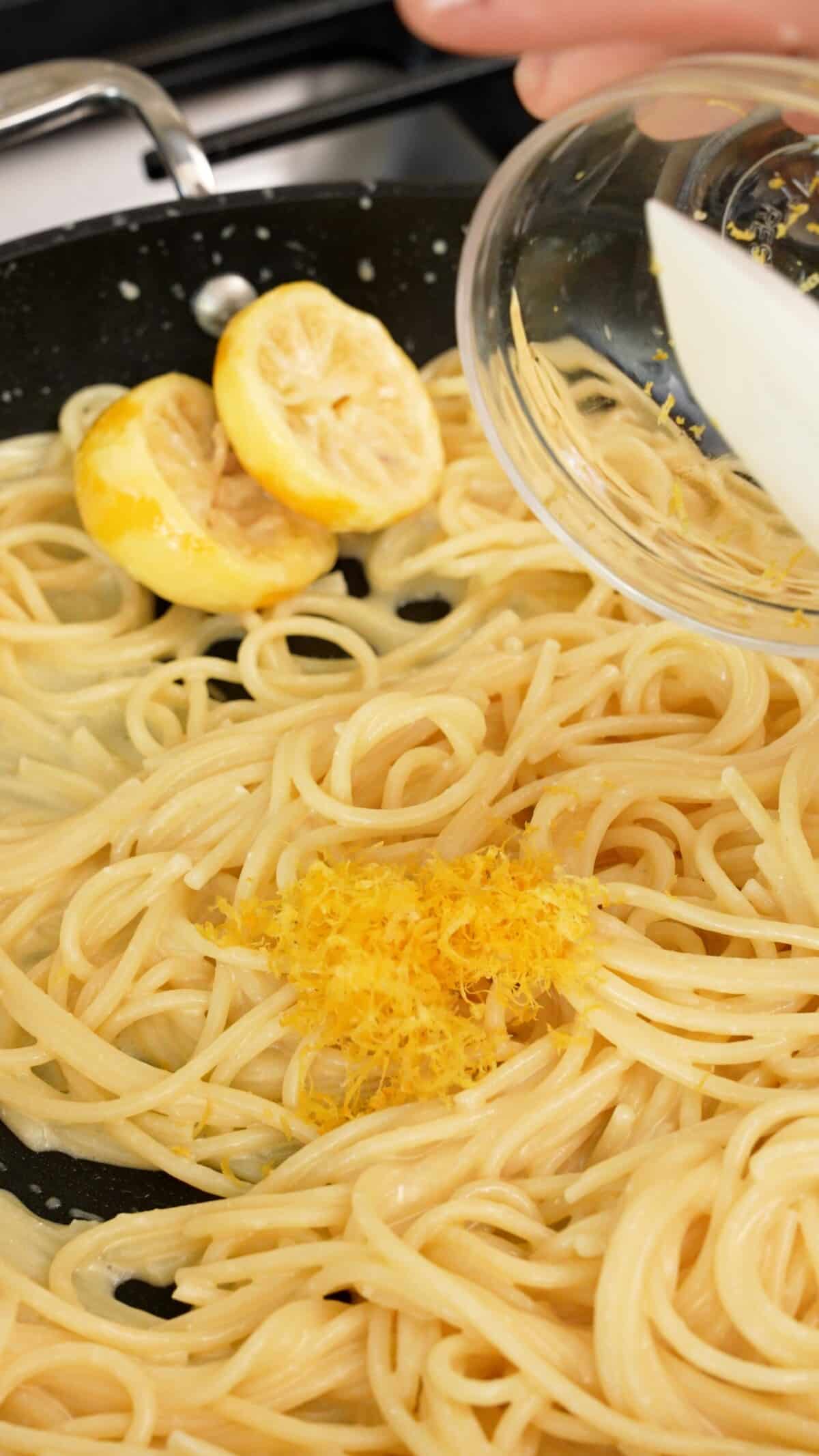 Lemon zest being added to pasta in a pan.