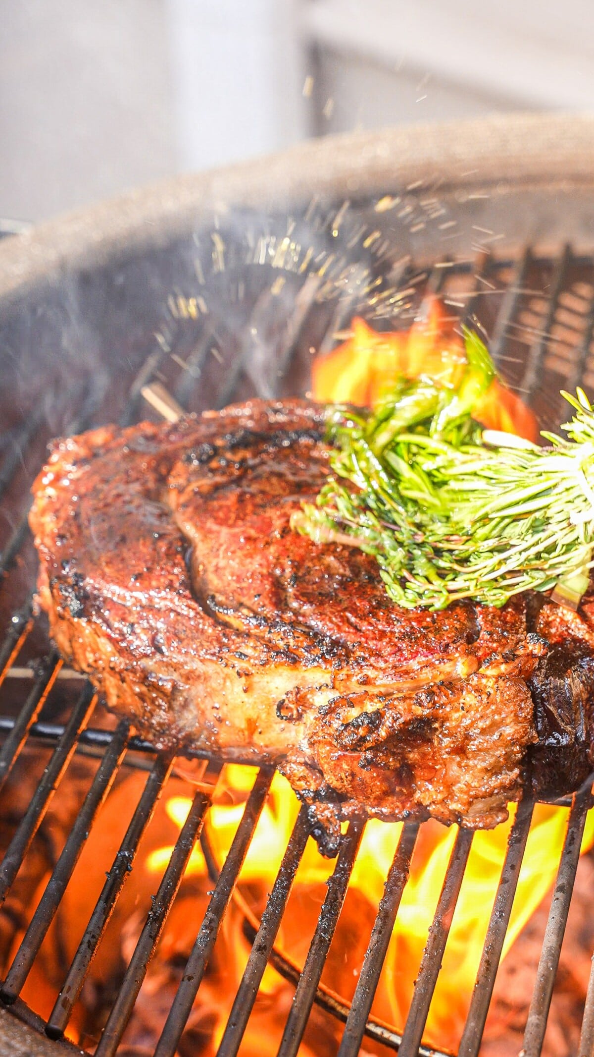 Grilled steak on a grill being basted with butter with an herb brush.