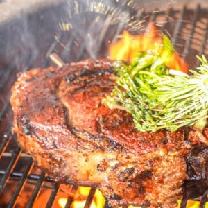 Grilled steak on a grill being basted with butter with an herb brush.