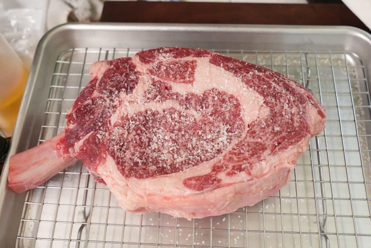 Raw ribeye steak being salted for a dry brine.